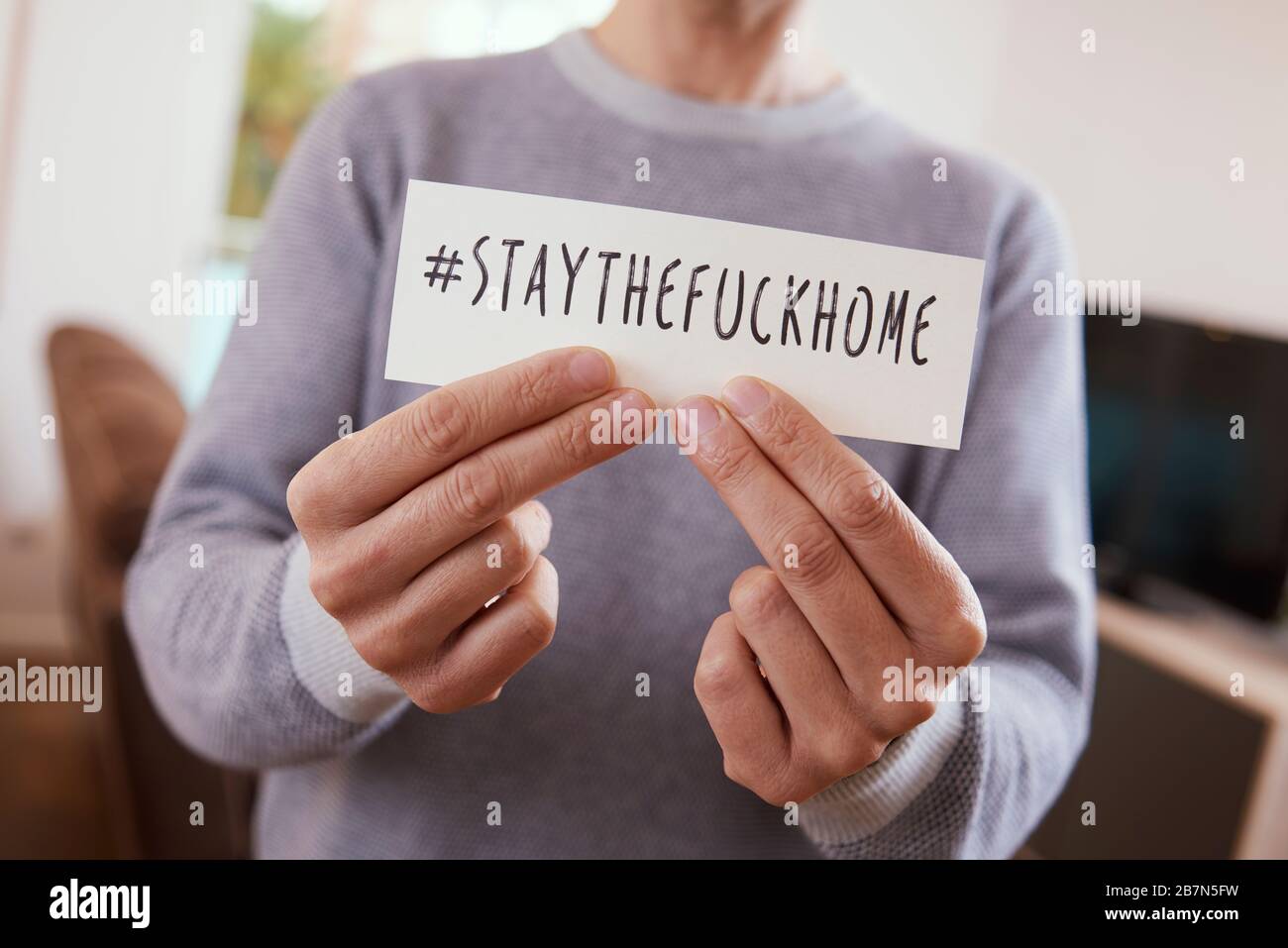 closeup of a man indoors showing the message #staythefuckhome written in a piece of paper, to alert of the need to stay as a measure to stop the sprea Stock Photo