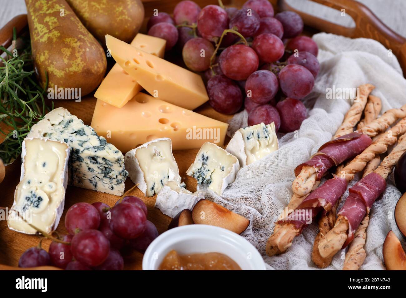 Antipasto. Dish with crispy grissini wrapped in sun-dried bacon, slices of brie cheese, camembert, blue cheese, radamer and muscat grape vine with fru Stock Photo