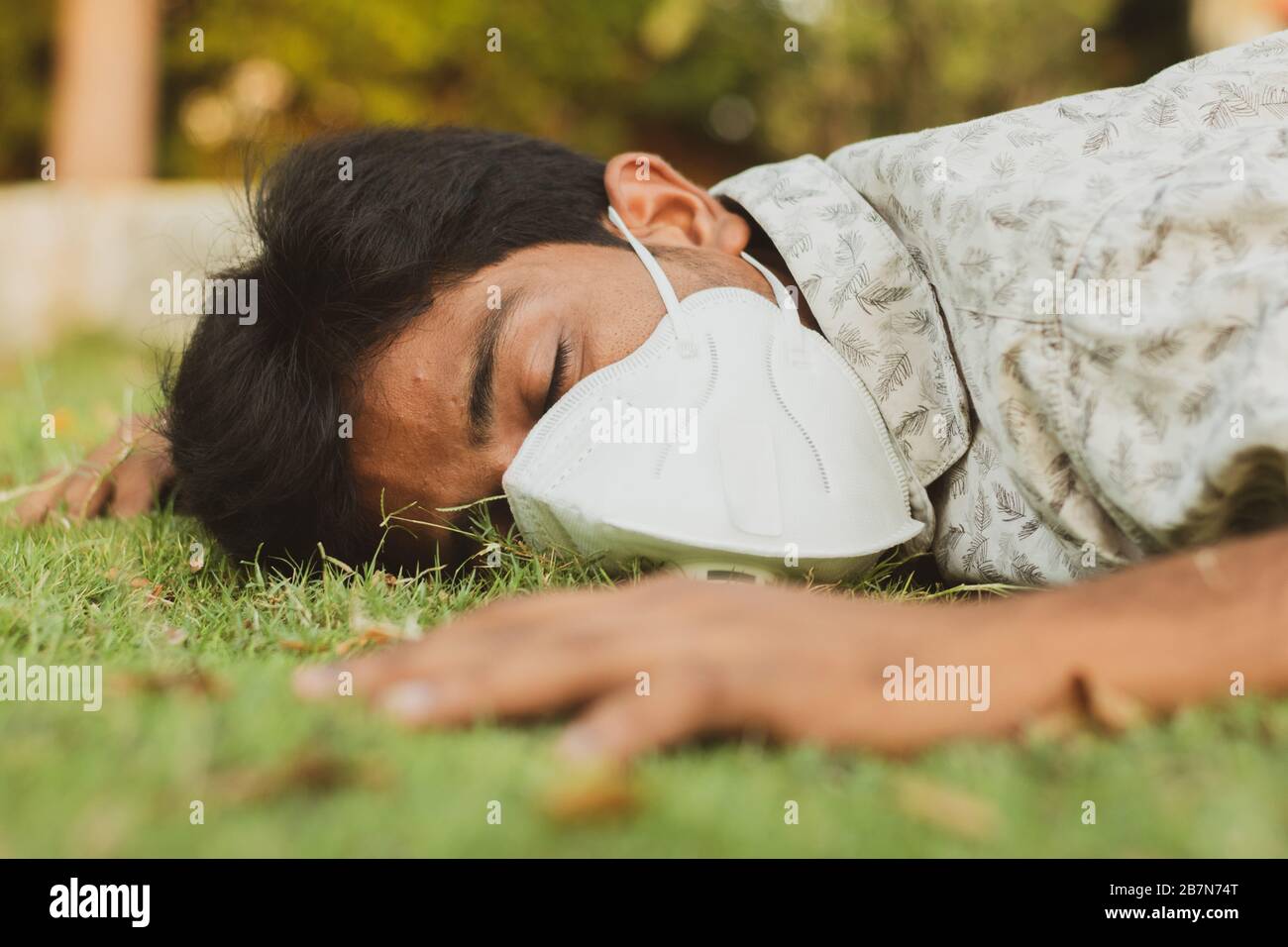 Sick young man fell down on ground with medical face mask - concept showing of sick, dizzy , ill health, dehydration or sun stroke. Stock Photo