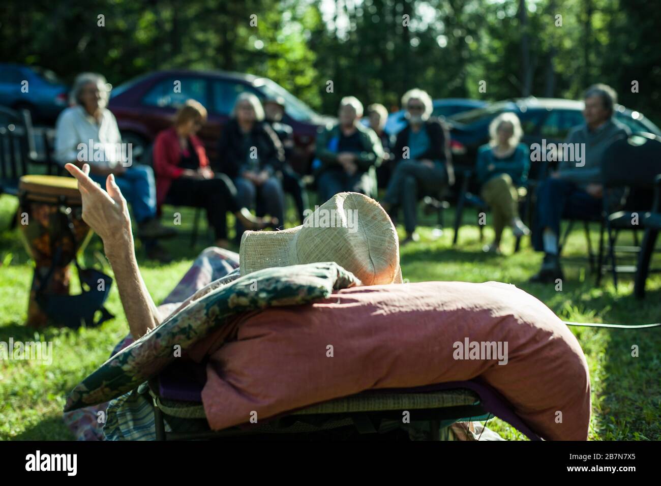 A close up shallow focus view from behind a terminally ill frail man lying on a sun lounger in garden during a party celebrating his life with copy space. Stock Photo