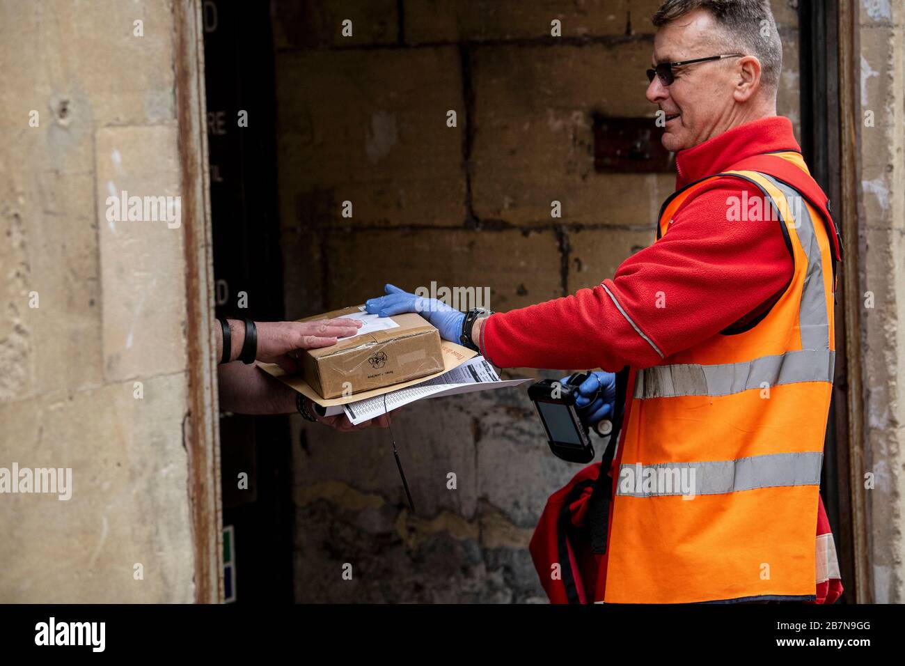 A Royal Mail postman makes deliveries wearing rubber gloves in Bath, Somerset, after the government announced stricter measures to combat Coronavirus. Stock Photo