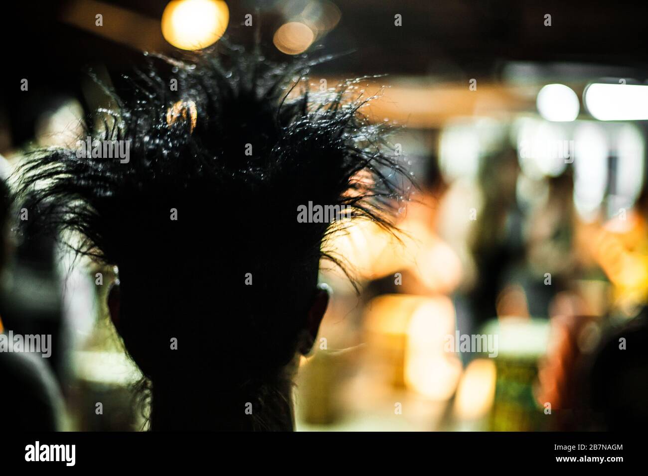 A close up backlit view of a person with a crazy hairstyle seen from behind. Spiky and styled hair silhouette in a club by night with copy space. Stock Photo