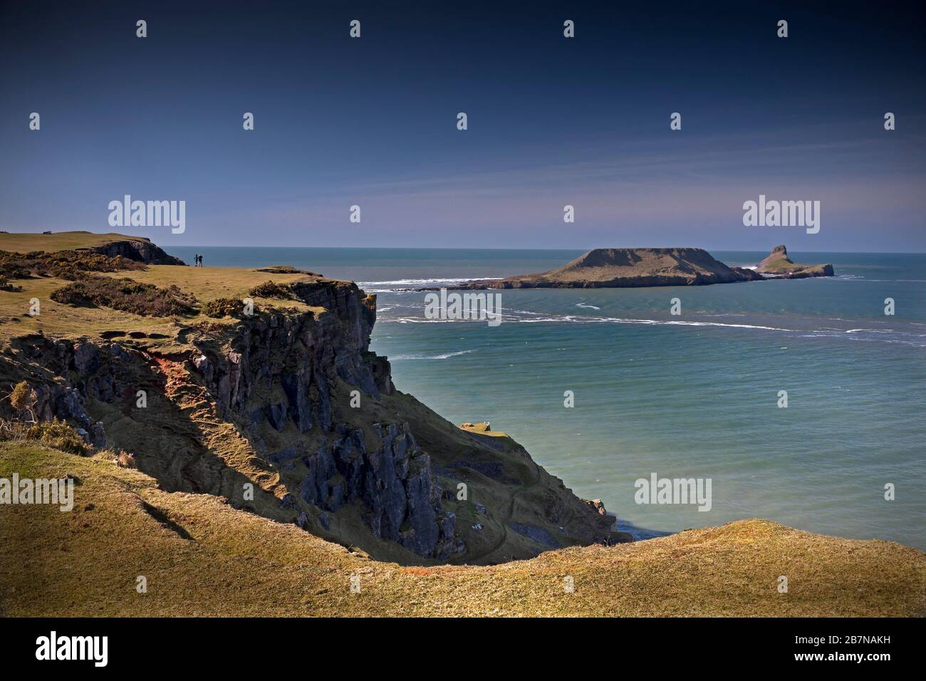 Worms Head at Rhossili on the Gower Peninsula with couple standing on clifftop, Wales,UK Stock Photo