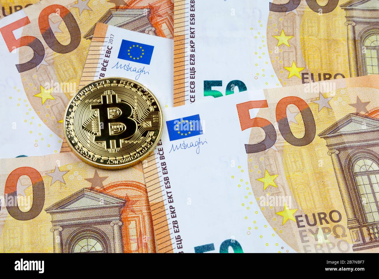 Close-up on a golden Bitcoin coin on top of a stack of 50 Euro banknotes. Stock Photo