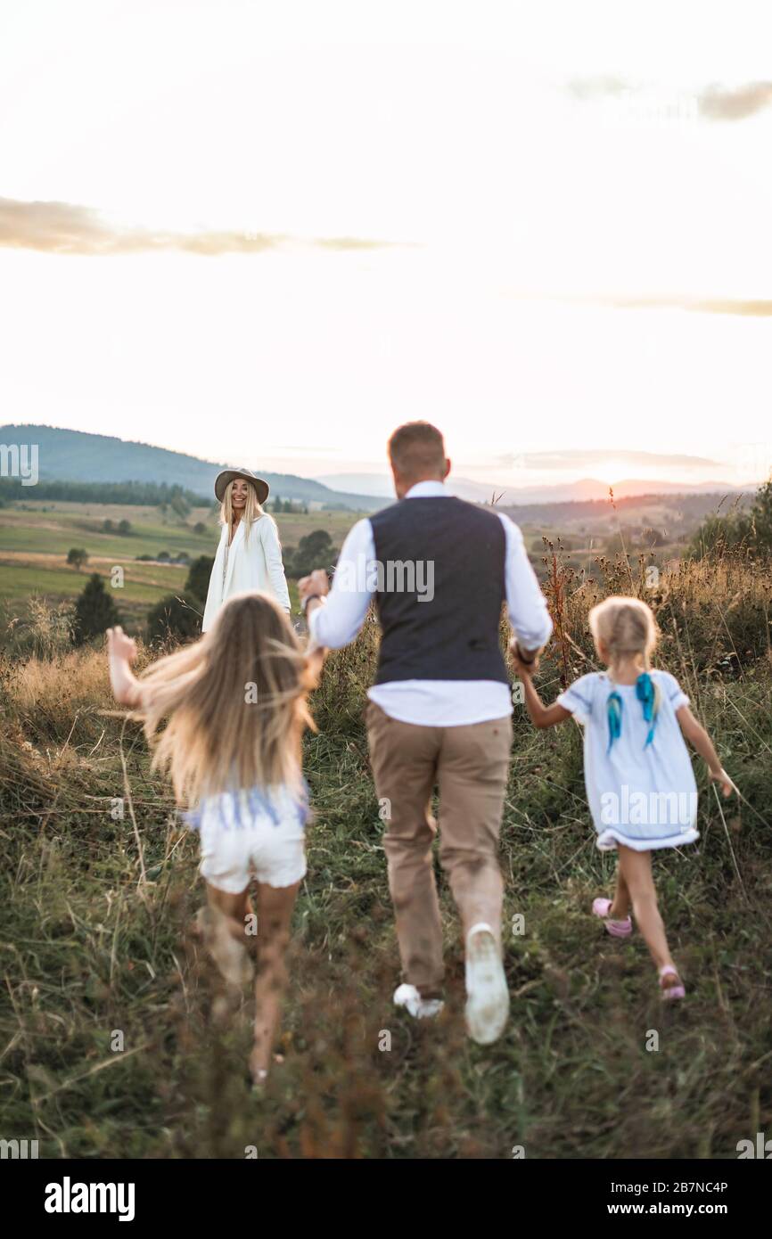 Stylilsh family, father, mother and two little cute daughters having fun and running in summer wild field. Stock Photo