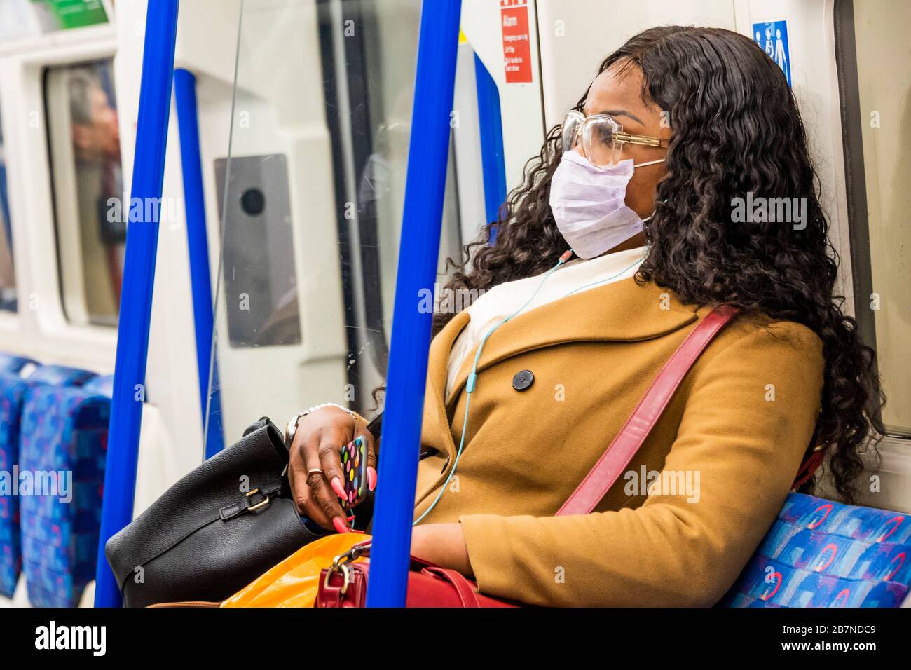 London, UK. 17th Mar 2020. A young black woman travels south at a safe distance from other passengers - Anti Coronavirus (Covid 19) defences, wearing inefectual masks on the Northern Line of London Underground. Credit: Guy Bell/Alamy Live News Stock Photo