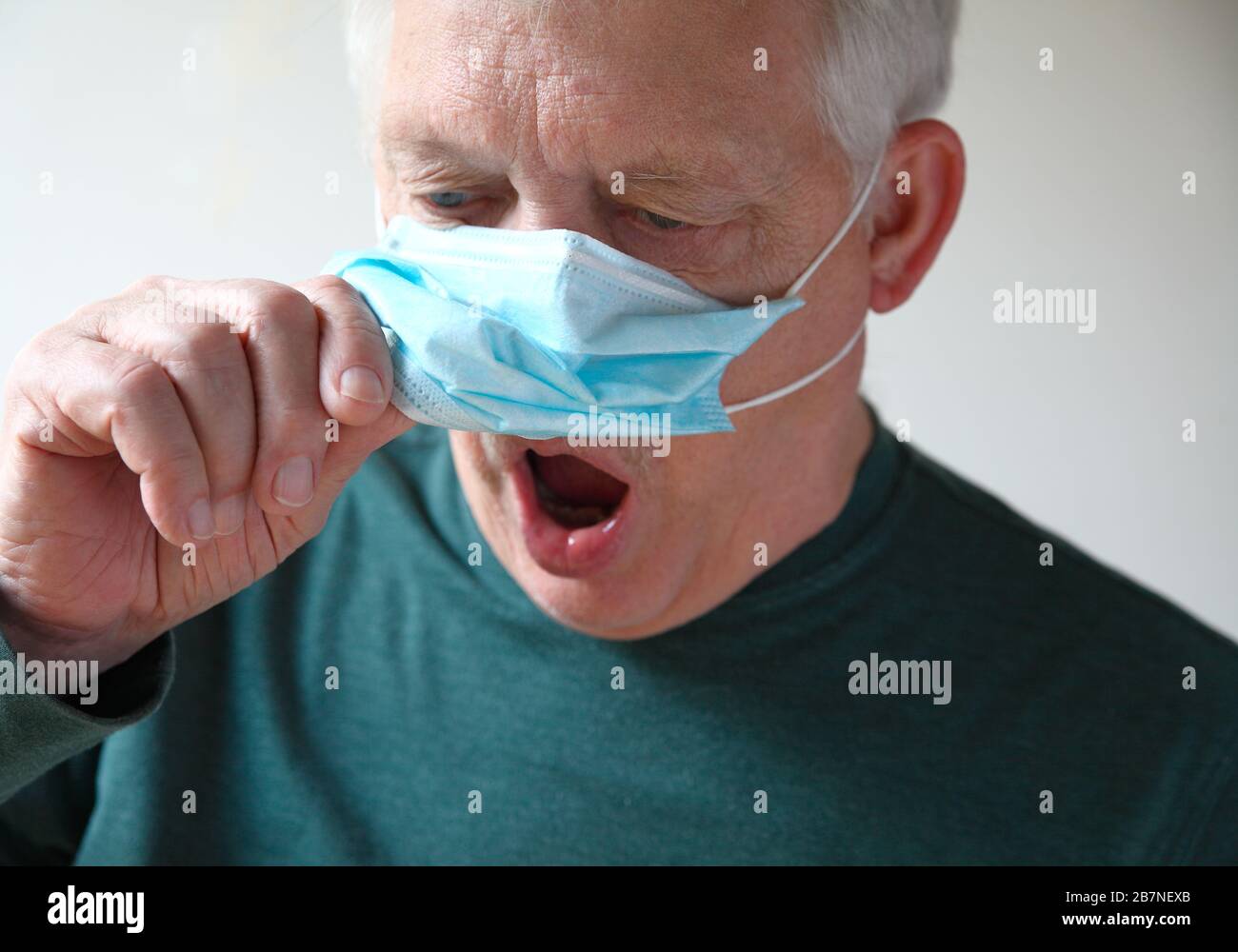 Senior man lifts his medical mask to gasp for air Stock Photo