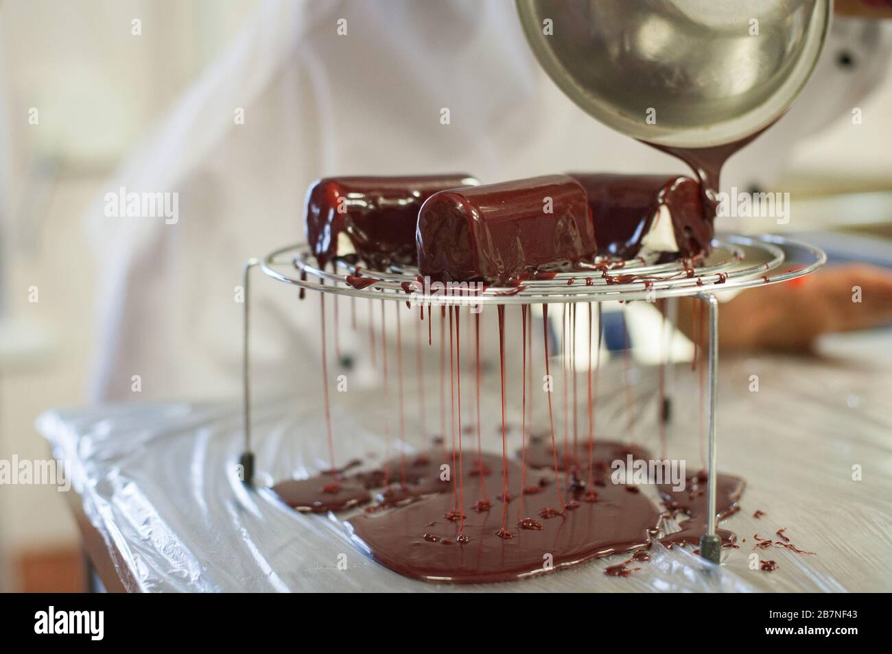 Confectioner pours dessert with chocolate icing. The process of making dessert in the kitchen Stock Photo