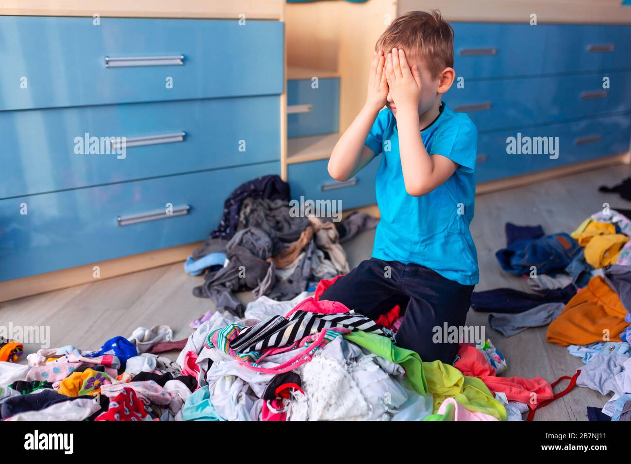 Small boy desperate with the mess in his clothes in his bedroom. Stock Photo