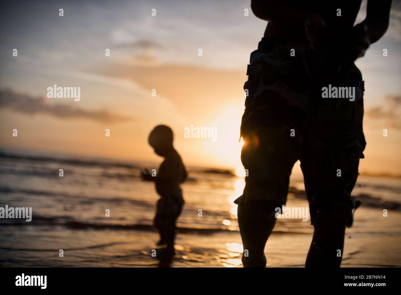 Young boy standing in water at the beach at sunset. Stock Photo