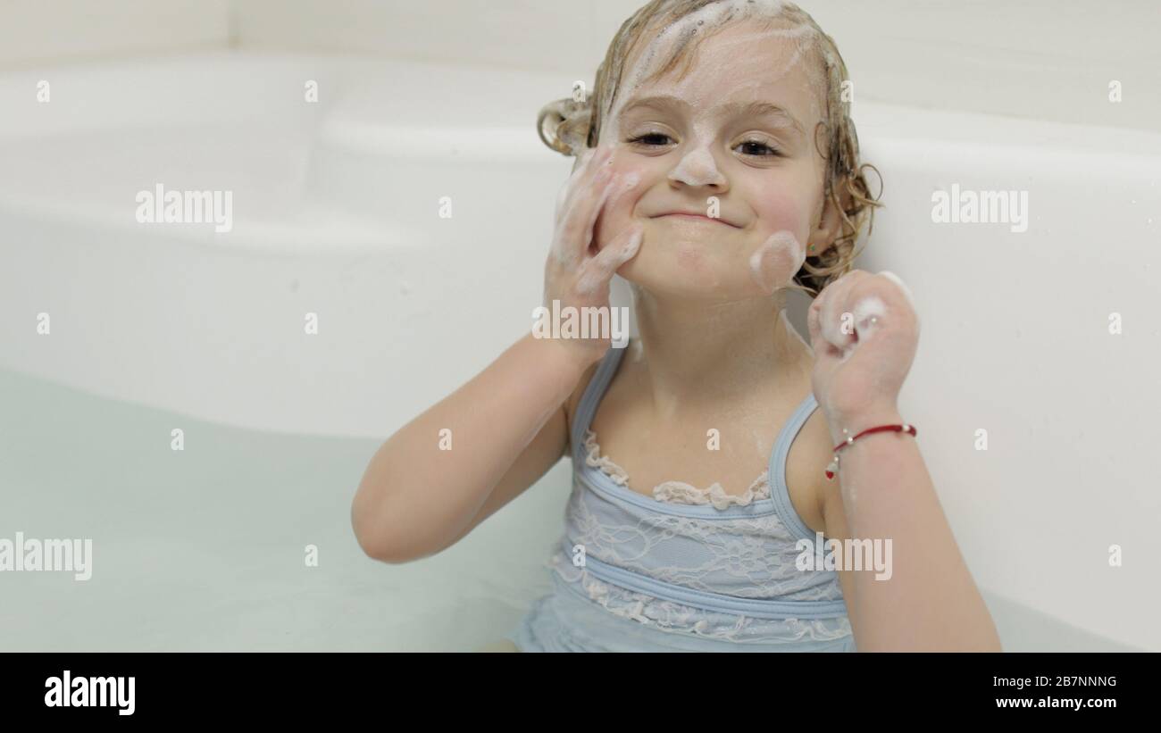 Attractive four years old girl takes a bath with bath foam in swimwear ...
