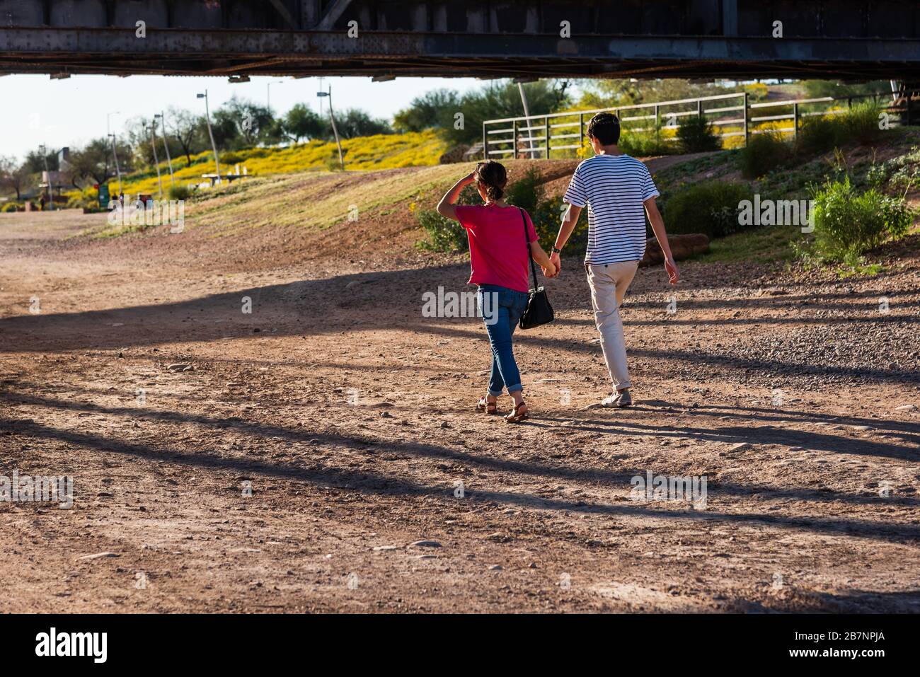 Young couple walking and holding hands at Tempe North Shore Beach, under the Tempe Bridge. Stock Photo