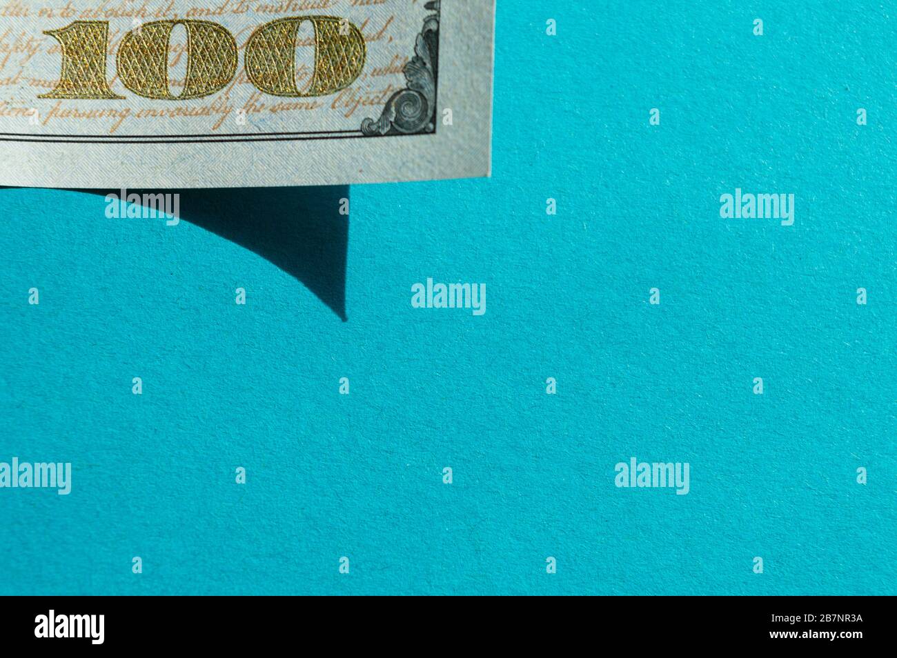 Piece of 100 dollar bill at the upper-left corner on the bright blue background. Conceptual photo, minimalistic design Stock Photo