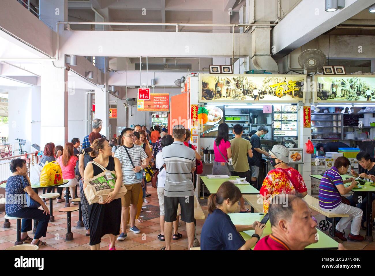 People queue up and eat food in a hawker centre in Singapore Stock
