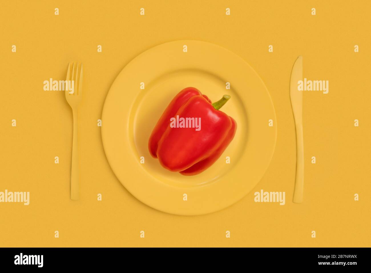 Red bell pepper on top on a yellow plate, knife and fork. On yellow background. The view from the top. Stock Photo