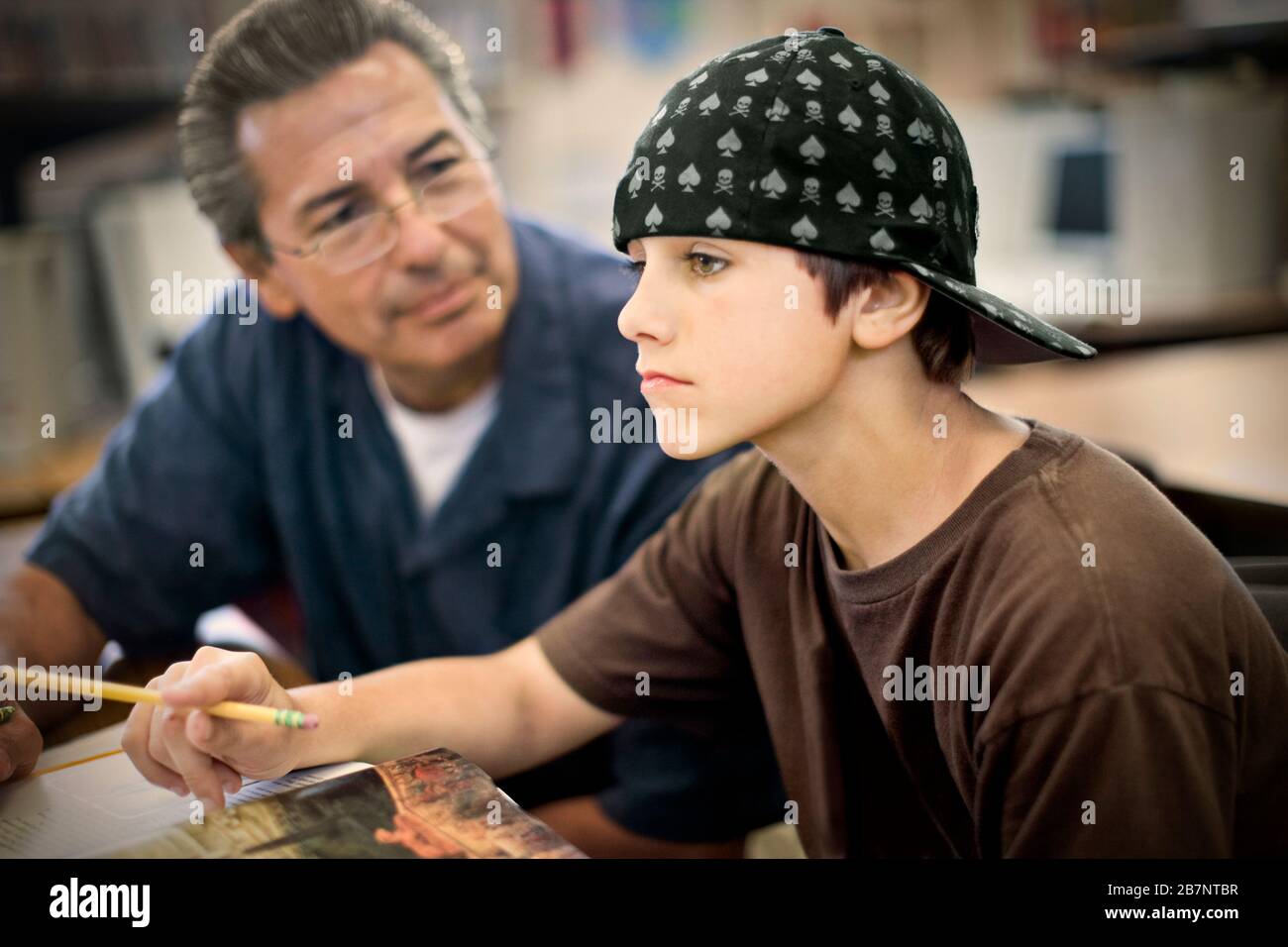 Teenage boy sitting in class with a mature adult male teacher. Stock Photo