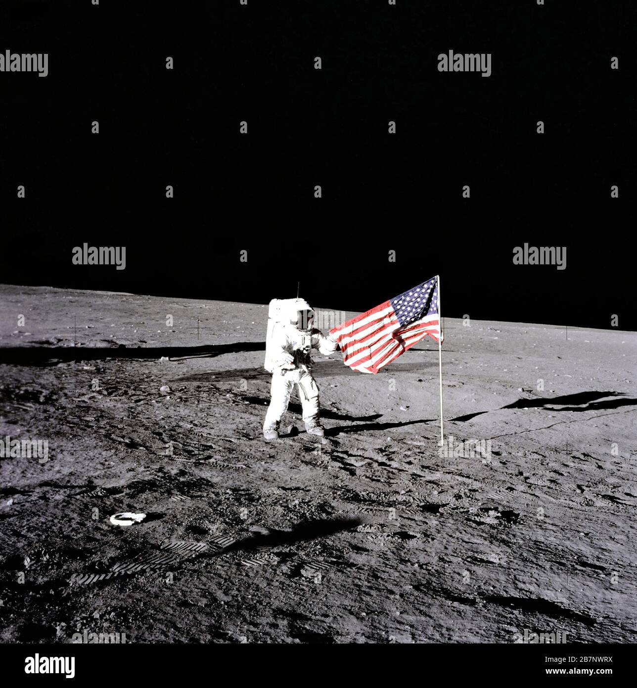 Apollo 12 - NASA, 1969. During the first extravehicular activity, astronaut Charles Conrad, Jr., Apollo 12 commander, releases the United States flag on the lunar surface. Boot prints from the astronauts can be seen in the image as well, November 19, 1969. Stock Photo