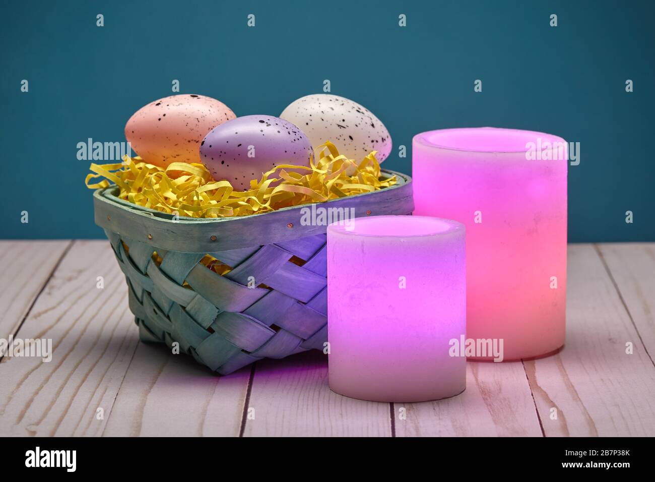 Two Glowing Pink Wax Candles and a Basket of Easter Eggs Stock Photo