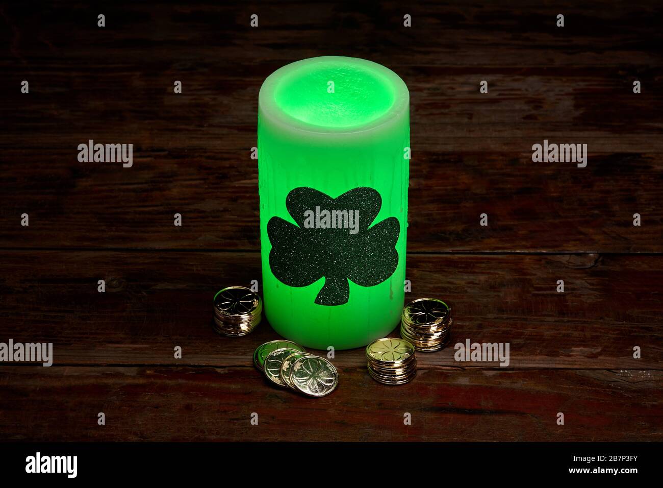 Glowing green wax candle and stacks of gold coins for St. Patrick's Day Celebration Stock Photo