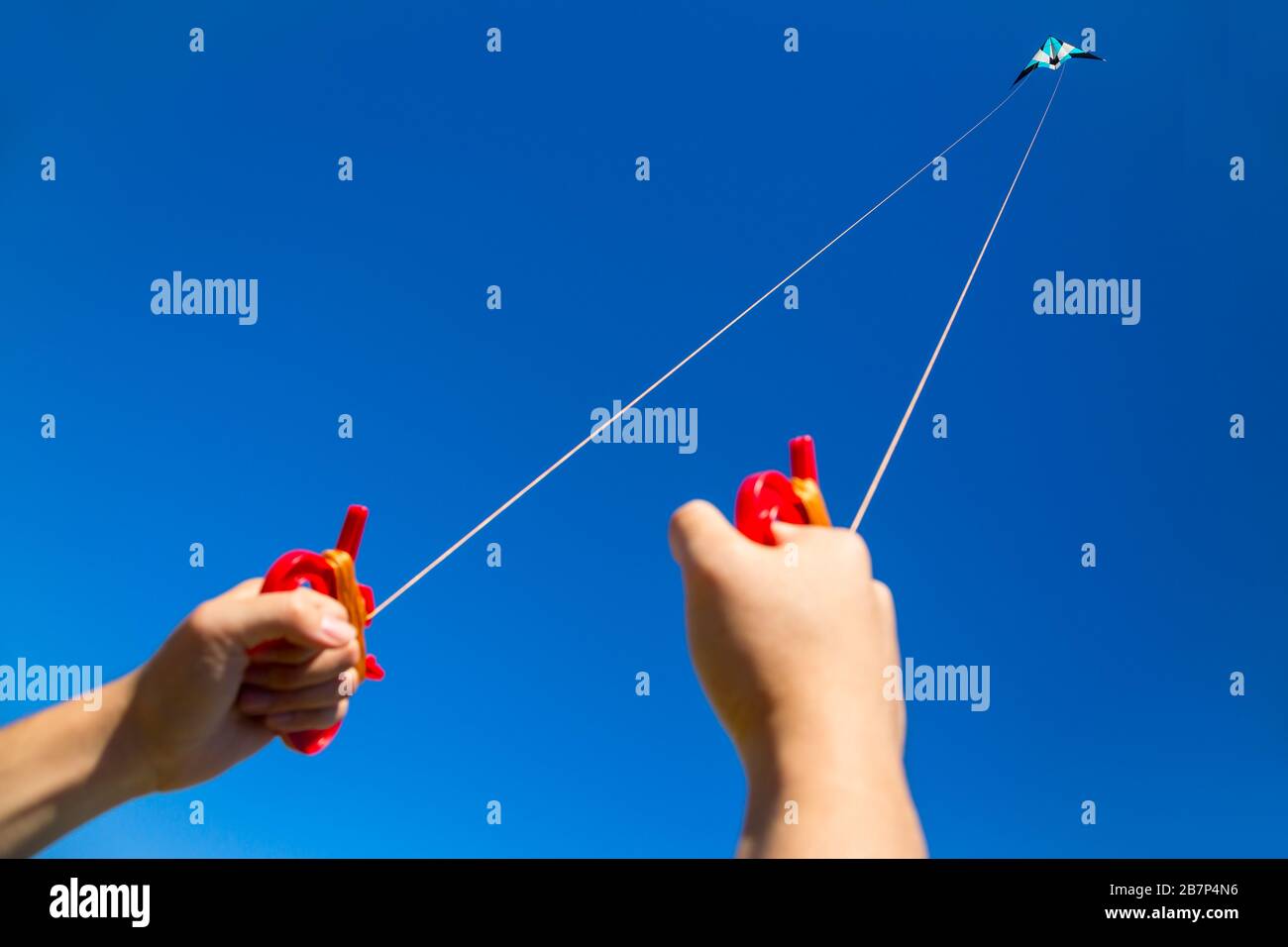 Two male hands holding kite strings with a kite  in sky at distance Stock Photo