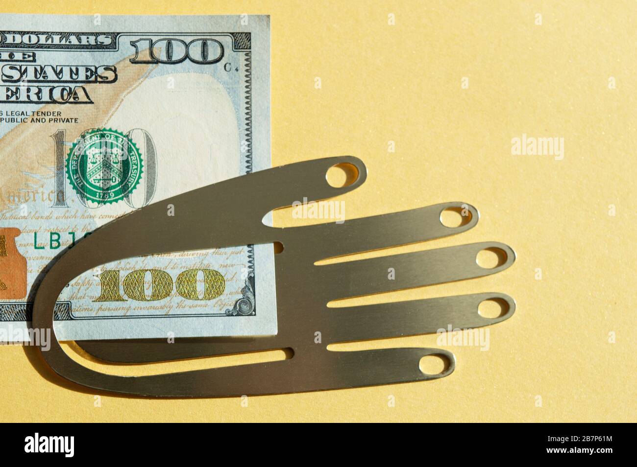One hundred American dollar bill, holding by metal hand on the golden background. Conceptual photo, minimalistic design Stock Photo