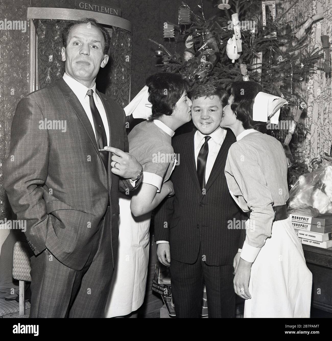 1960s, historical, famous British boxers, Henry Cooper and Terry Spinks visiting a hospital at Christmas time in Lewisham, South East England, UK, with two females giving a kiss to Terry and Henry asking what about me. South East London born Henry Cooper was a hugely popular sportsman in Britain and later became the first and only British boxer to be knighted. Stock Photo