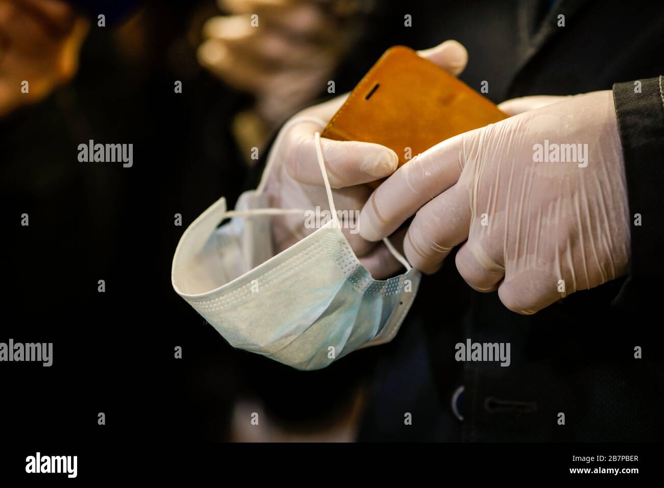 Details with the hands of a man in surgical gloves holding a mobile phone and a face mask to prevent the COVID-19 spread. Stock Photo