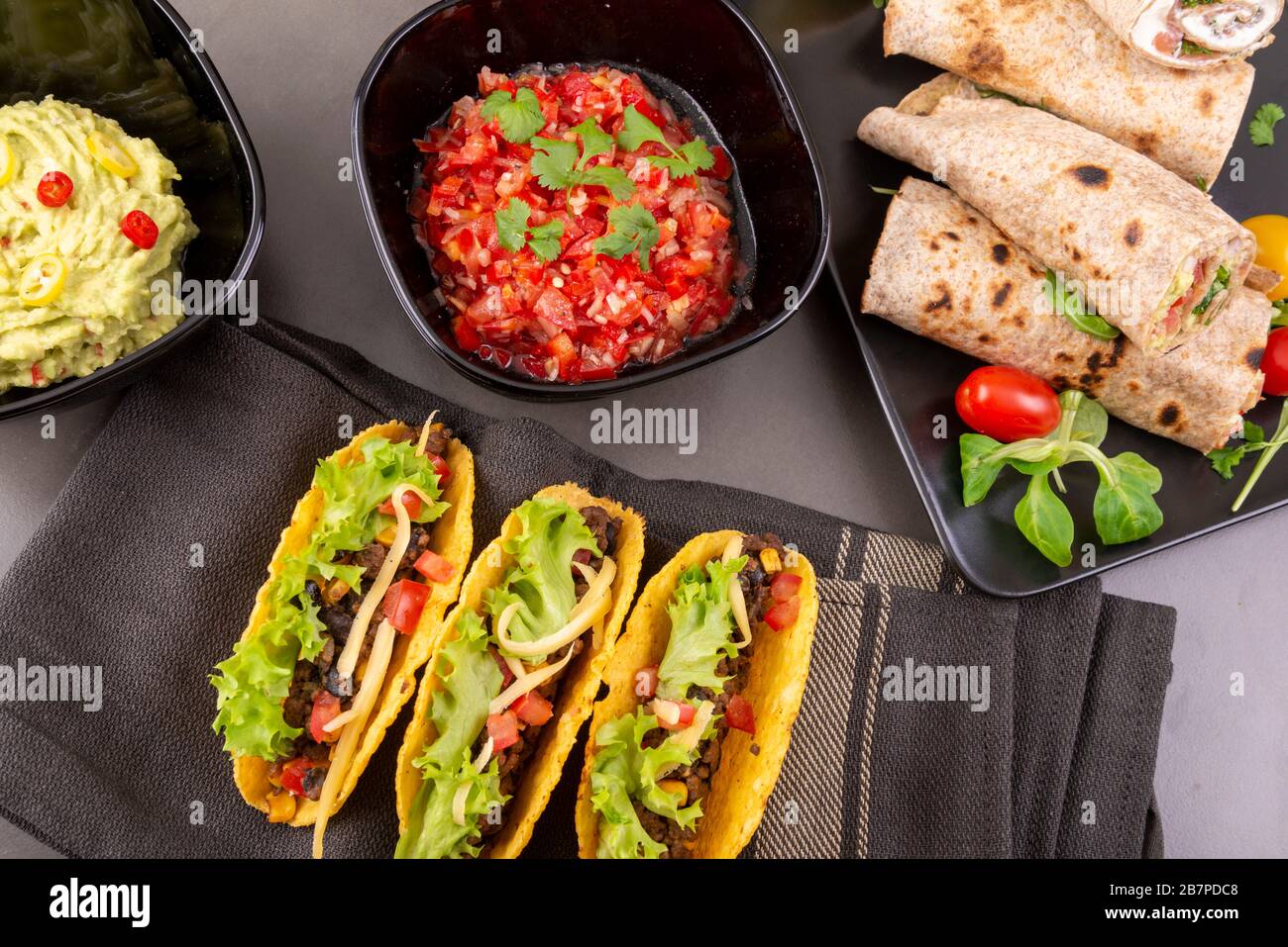 Various mixed Mexican dishes. Tacos, burritos, fajita, salsa, nachos on a dark table. Top view Stock Photo