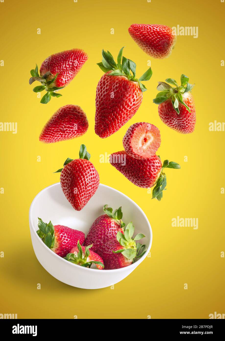 Strawberries flying in white bowl isolated from the background - yellow vertical image Stock Photo