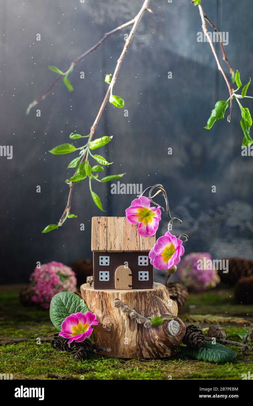 Miniature wooden toy house cottage with pink flowers on moss background, spring Easter, Earth Day postcard concept Stock Photo