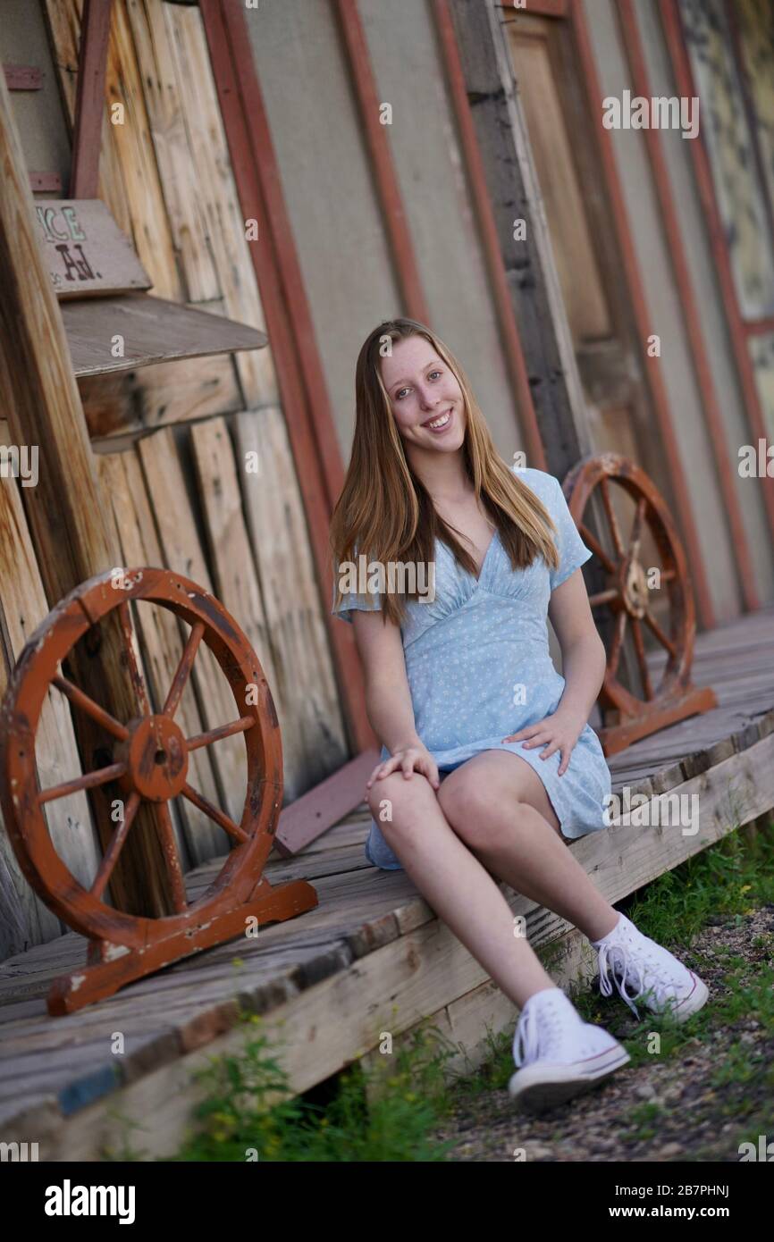 A teenage girl in a blue dress poses In front of a wood wall backdrop. Stock Photo