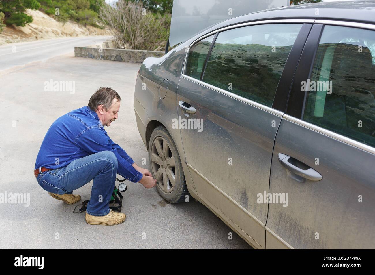 An elderly man pumps the wheel of a dirty car. Breakage on the road Stock Photo