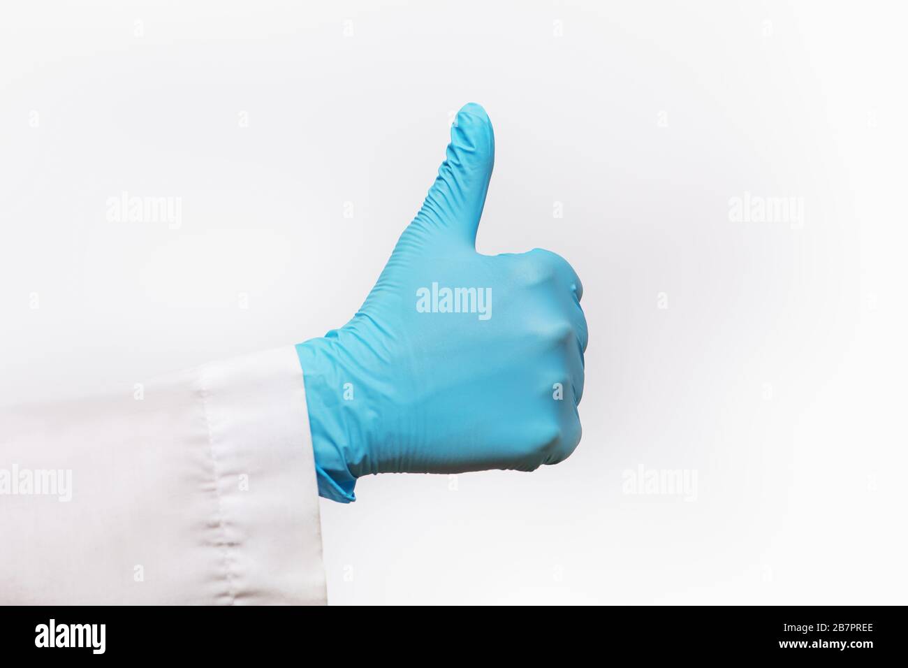 Partial view of hand wearing blue latex glove giving thumbs up on white background. Stock Photo