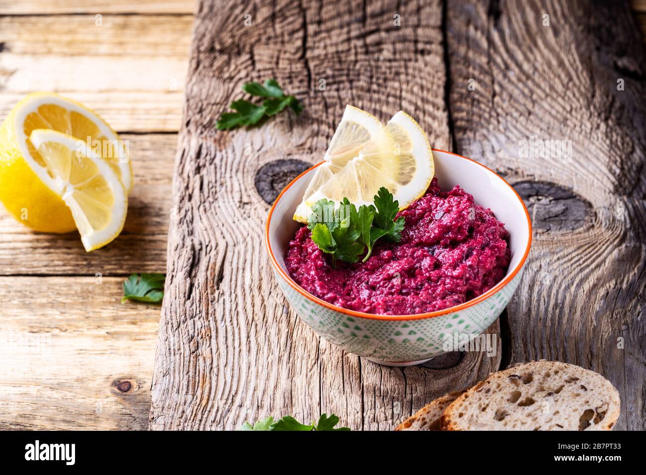 Beetroot hummus with horseradish and lemon juice, served on plate with fresh parsley herbs and whole grain seeded bread on rustic wooden table, plant Stock Photo