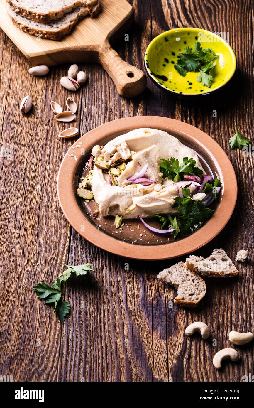 Healthy vegan snack hummus dip with nuts and herbs in ceramic bowl, close up Stock Photo