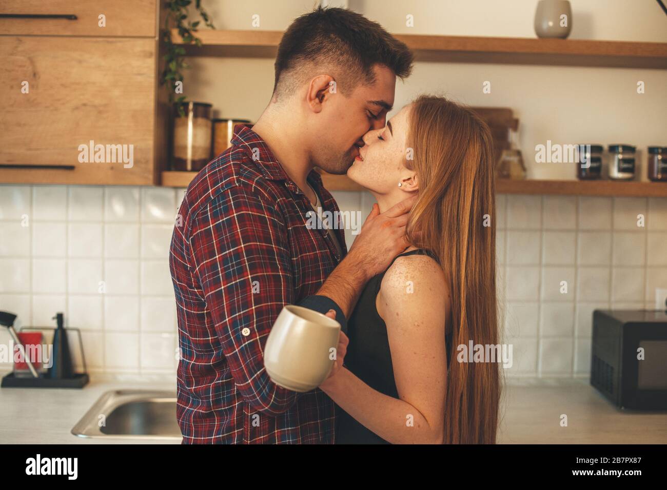 Lovely ginger woman with freckles is kissing her lover while drinking a cup  of tea in the kitchen Stock Photo - Alamy