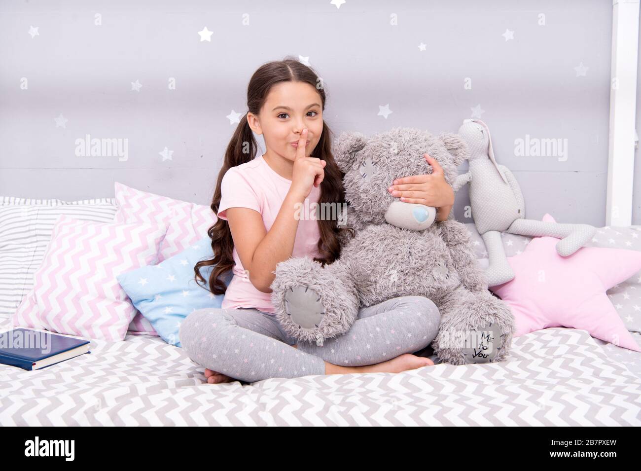 Girls secret. Cute kid show silence finger gesture. Little secret. Small girl play with teddy bear in bed. Keeping mouth shut. Being quiet. Silence and shushing. Top secret. Can you keep secret. Stock Photo