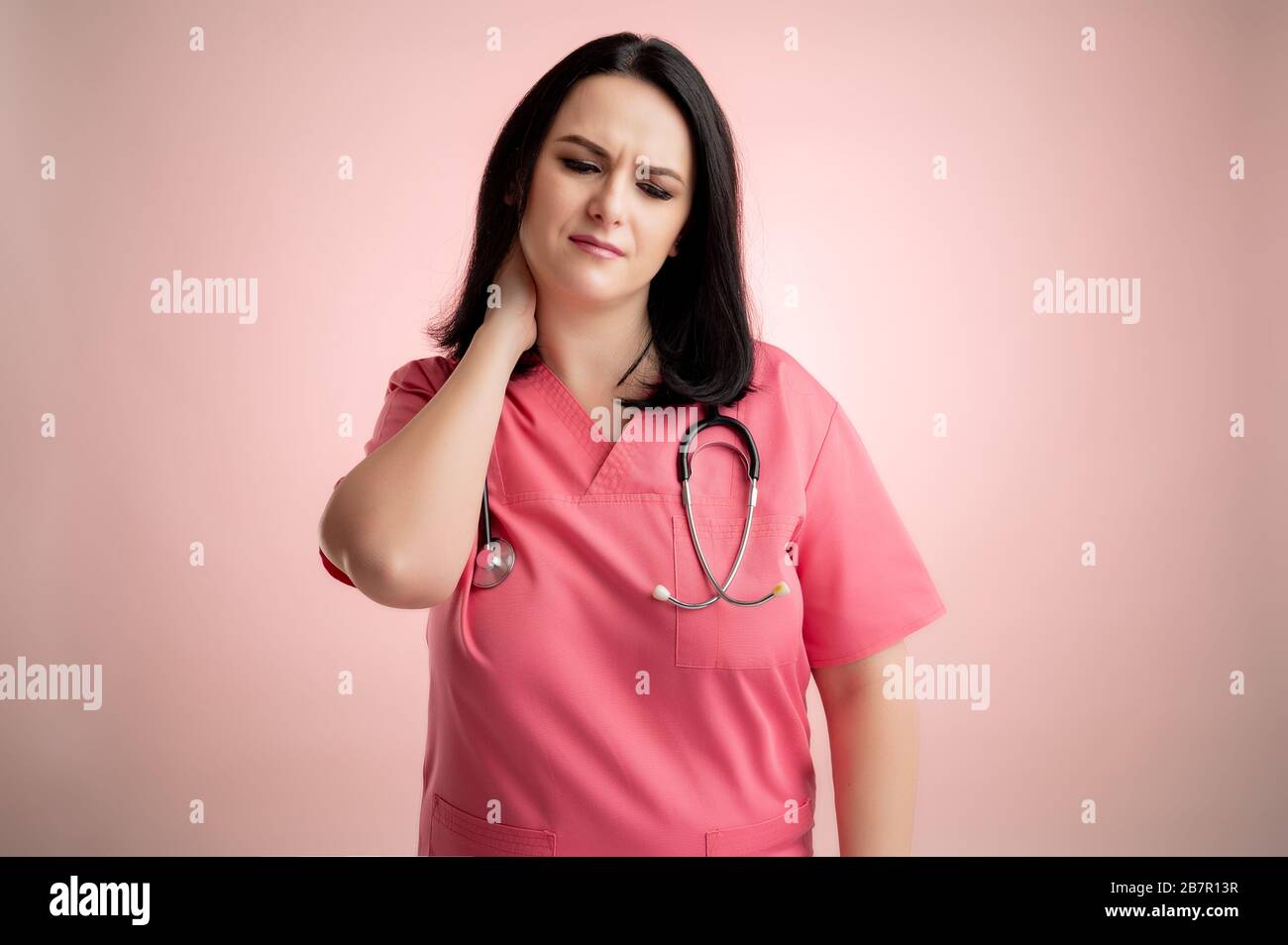 Portrait of beautiful woman doctor with stethoscope wearing pink scrubs, with open arms looking up, has sore throat posing on a pink isolated backroun Stock Photo