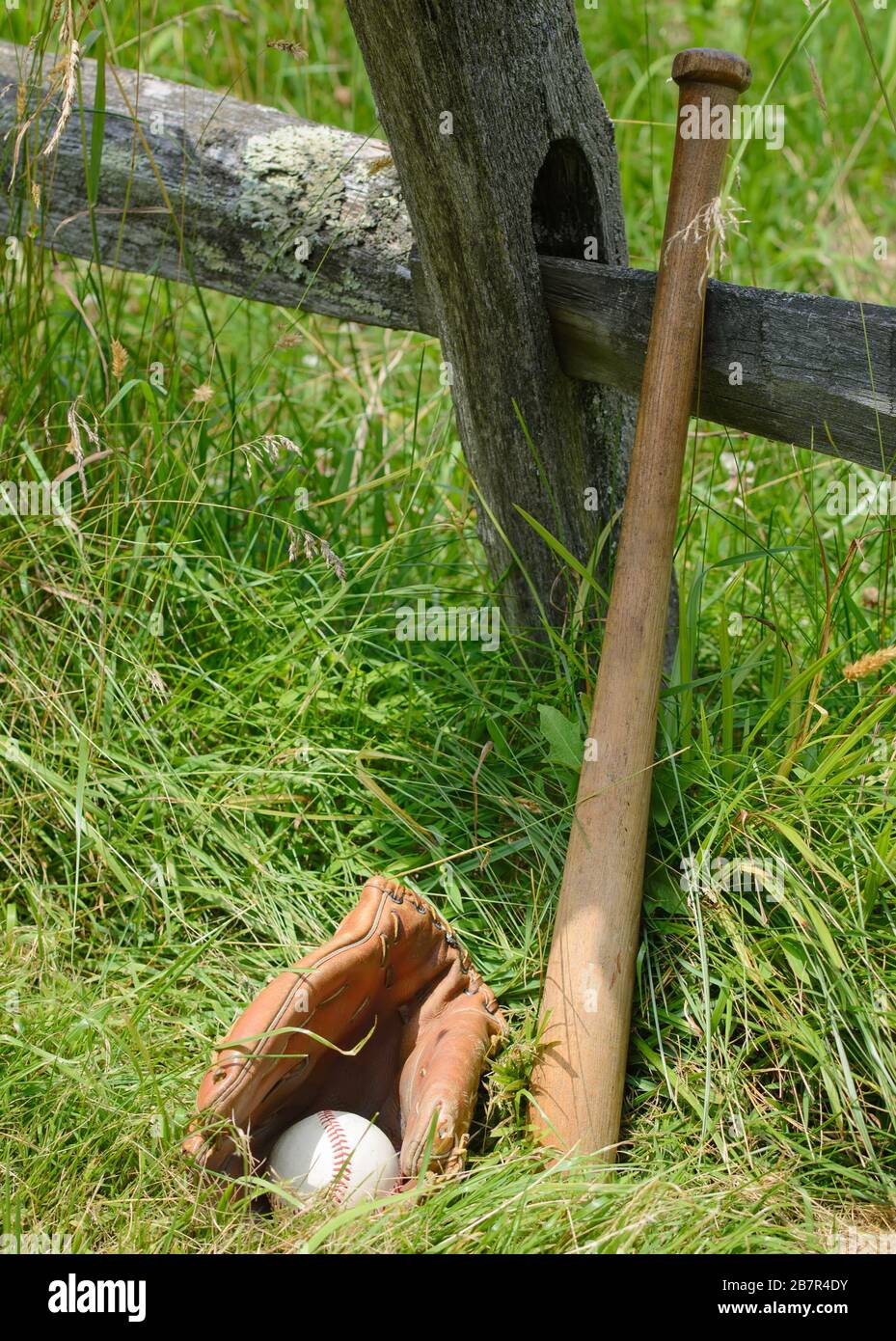 Baseball glove with ball inside and a bat leaning against a an old post. Stock Photo