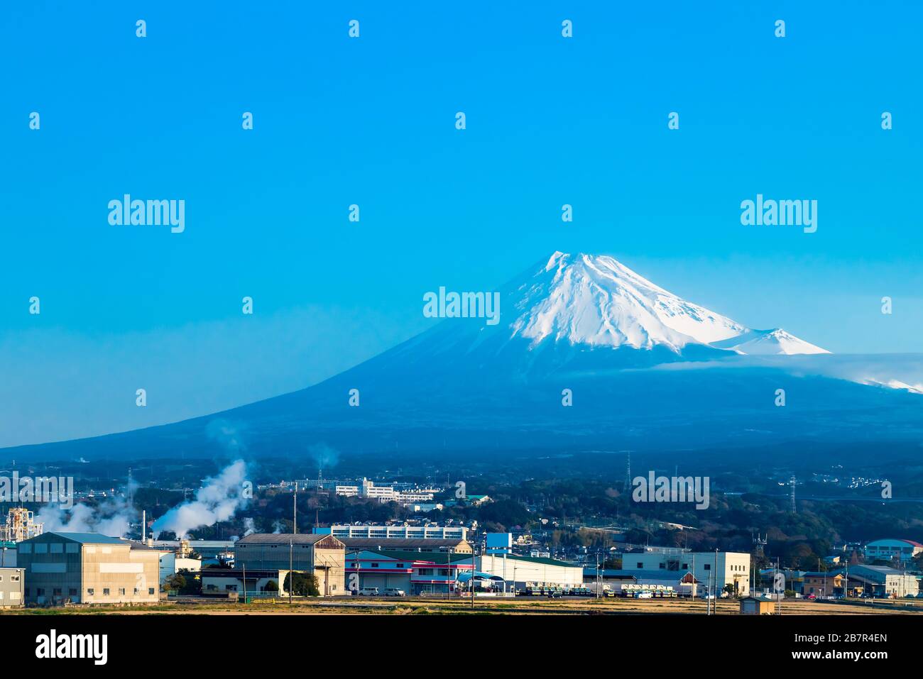 Mountain Fuji in Japan during day time with buildings in foreground, and with blue sky. Stock Photo