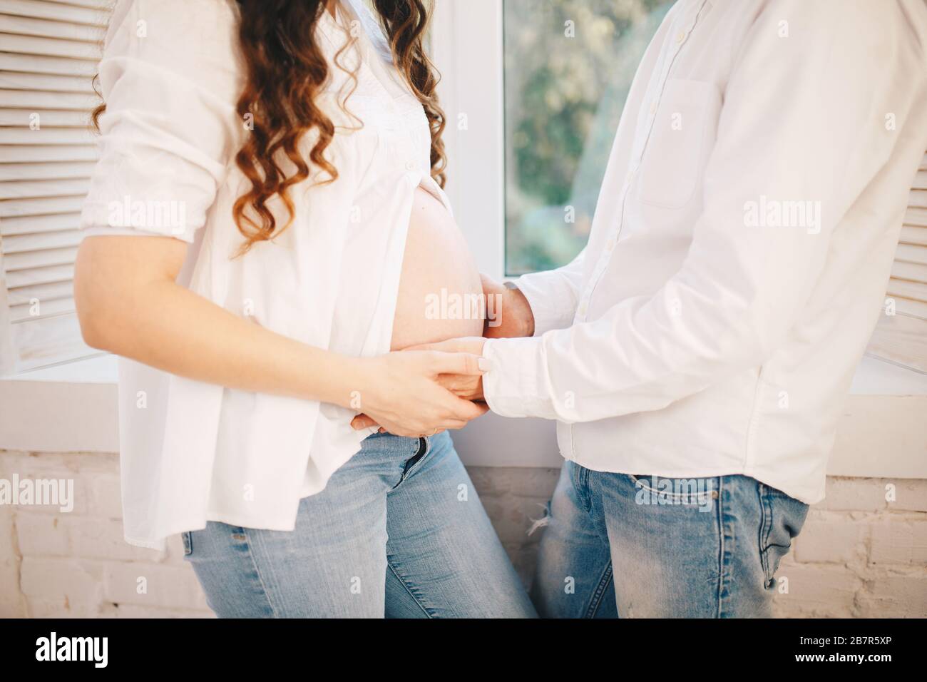 Woman opens her pregnant belly and man puts his hand on it Stock Photo