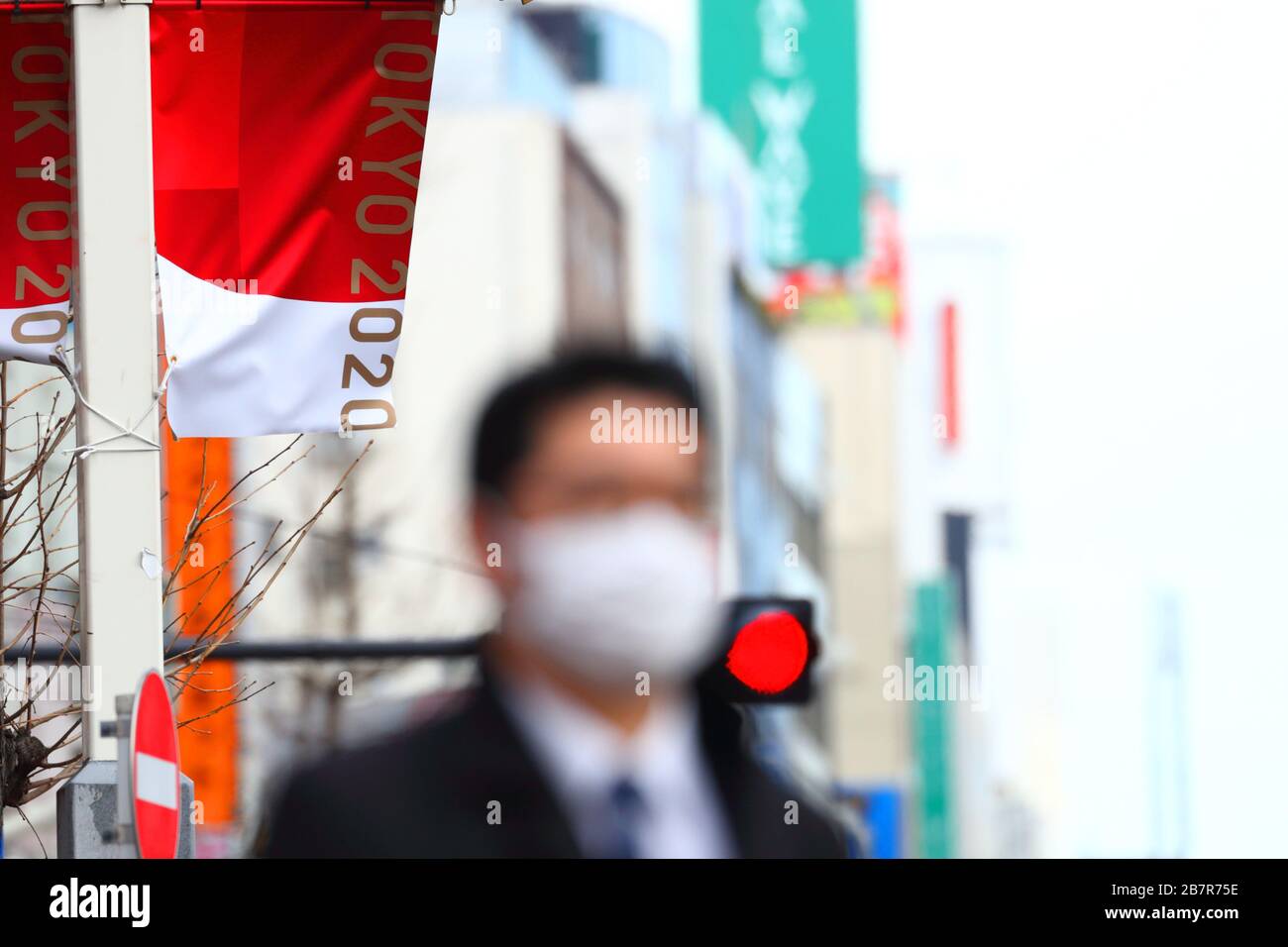 A man wearing a protective face mask walks in front of an Olympic Banner of Tokyo 2020 in Shinjuku, Tokyo, Japan on March 17, 2020. Credit: Naoki Nishimura/AFLO SPORT/Alamy Live News Stock Photo