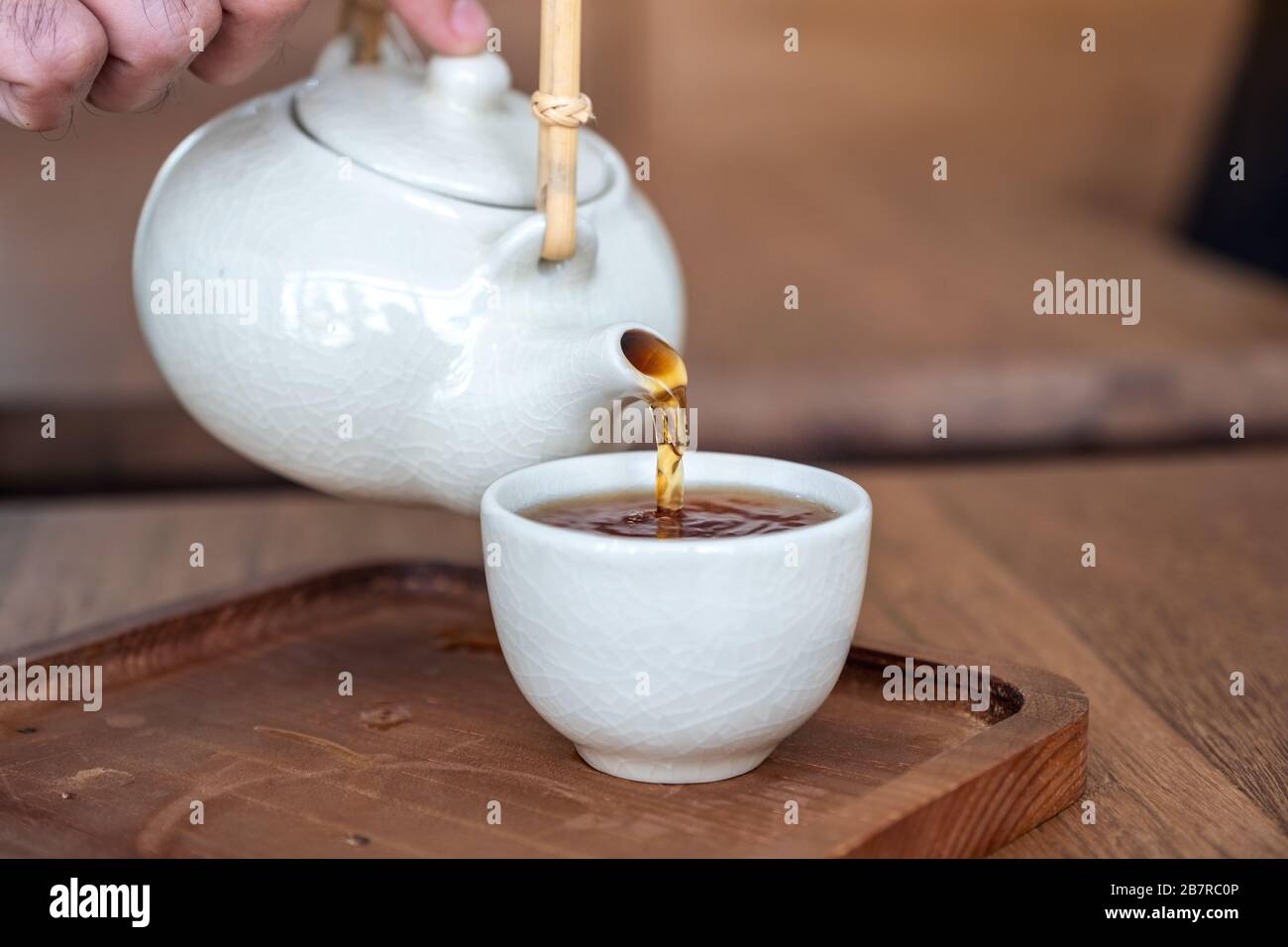 A hand pouring tea from ceramic japanese style teapot on wooden serving