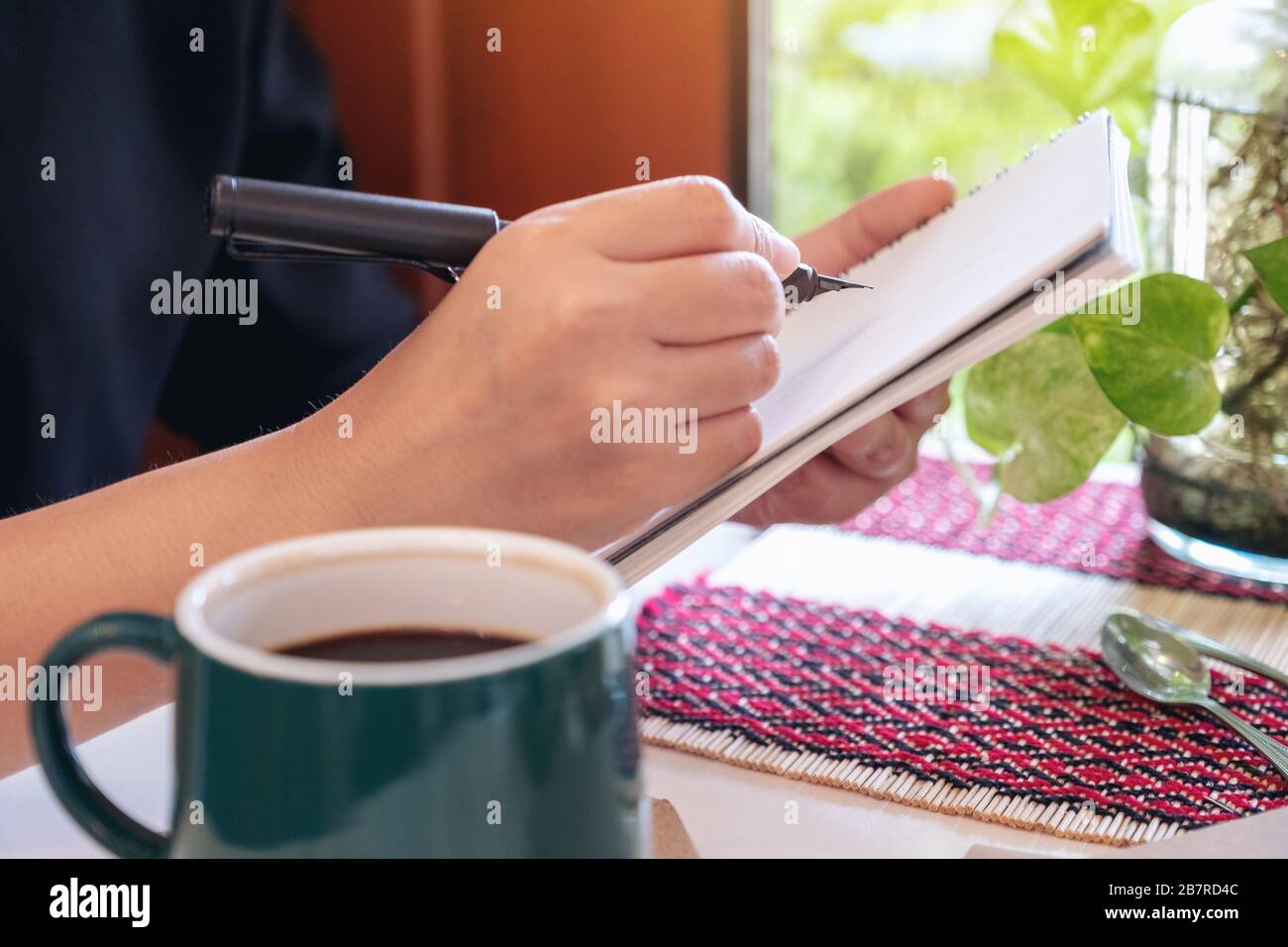 A woman holding and writing on notebook by fountain pen while sitting