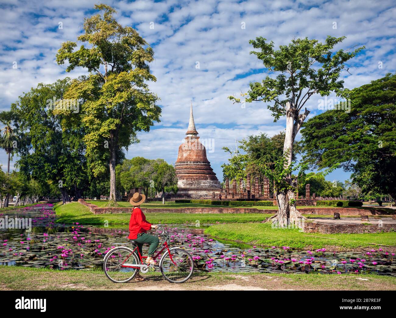 Woman in red shirt riding bicycle looking at old Buddhist temple in Sukhothai historical park, Thailand Stock Photo