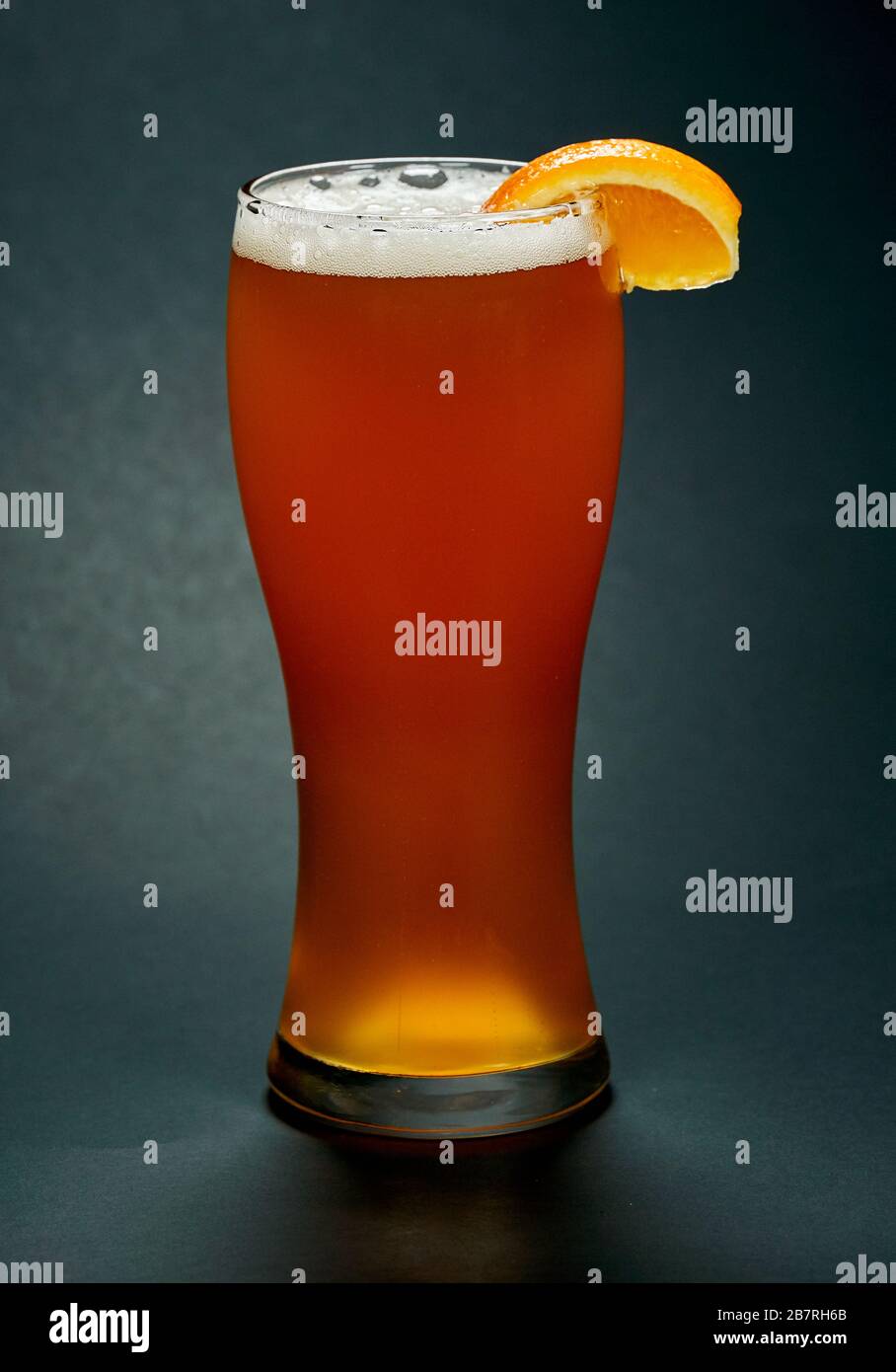 Glass of red beer with orange slice over black background. Beer is one