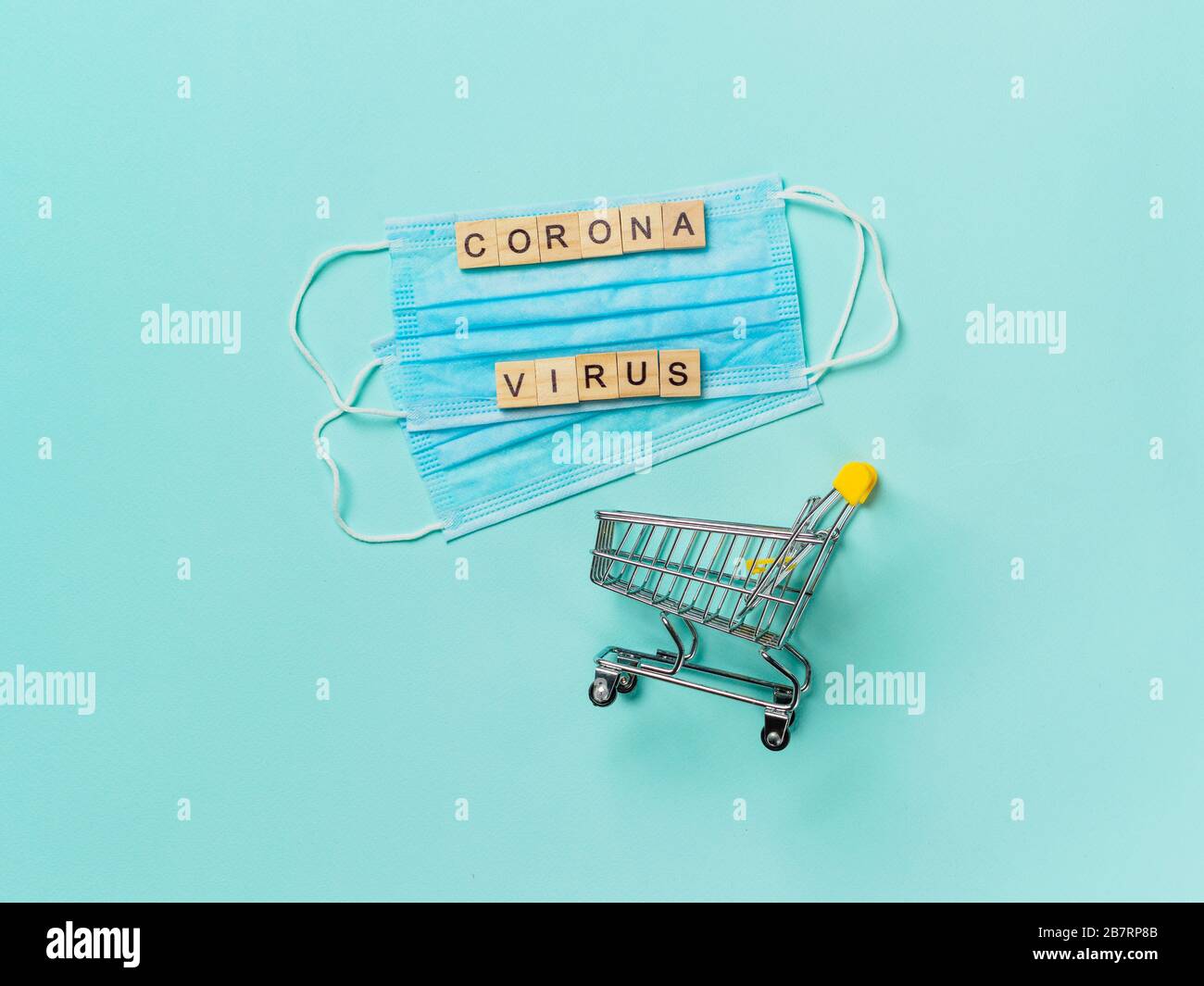 Coronavirus and shopping concept. Medical breathing mask and toy shopping trolley on blue background. Coronavirus concept top view. Copy space Stock Photo