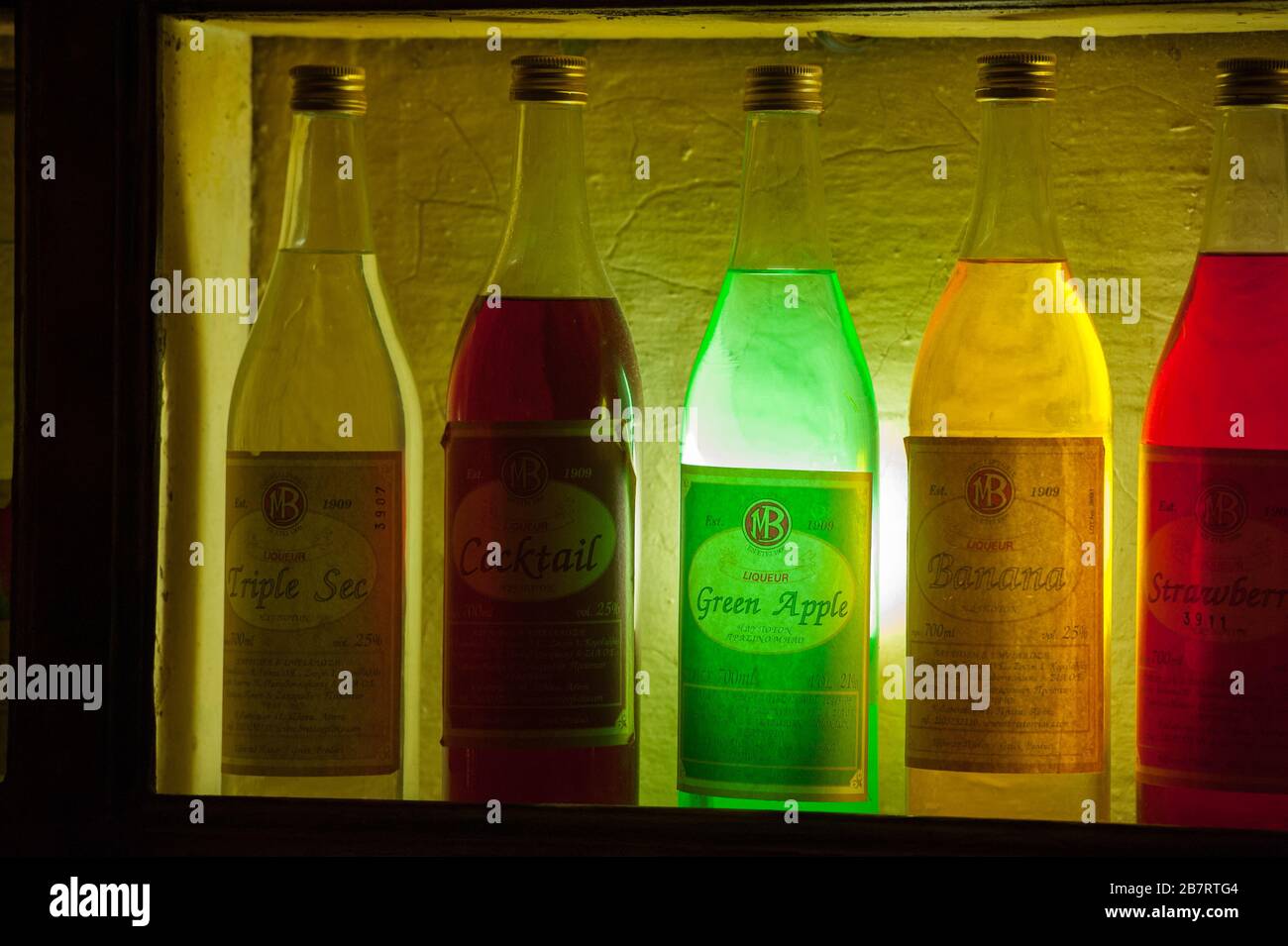 different coloured colourful liquor bottles backlit in bar in Athens Greece in bar at night green red and yellow liquid in clear bottles in Greece Stock Photo