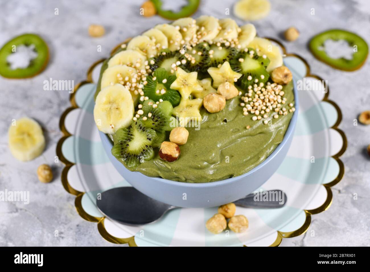 Green fruit smoothie bowl topped with star shaped banana, kiwi, hazelnut and puffed quinoa grain on gray background Stock Photo