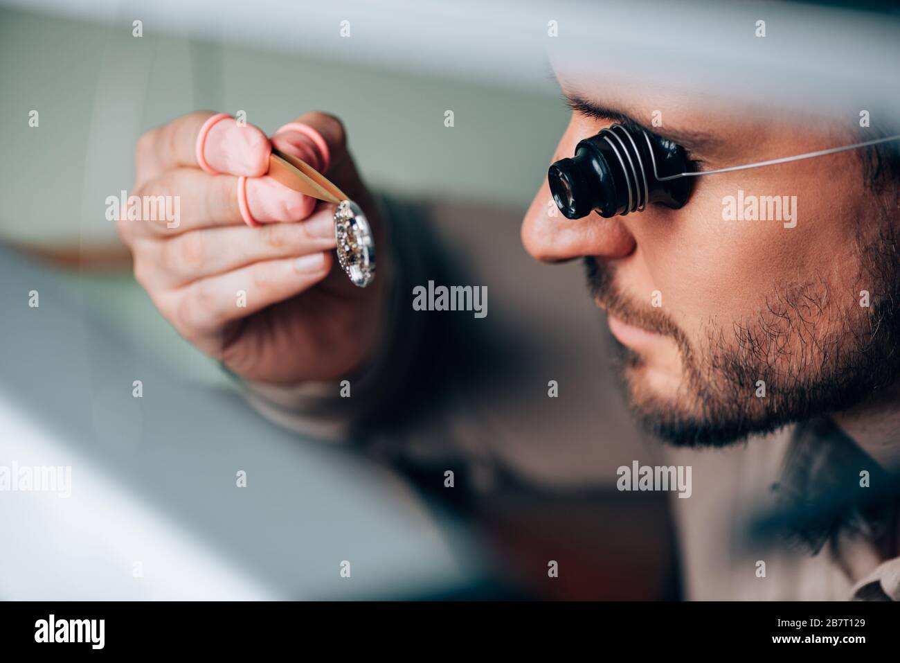 Side view of handsome watchmaker in eyeglass loupe looking at